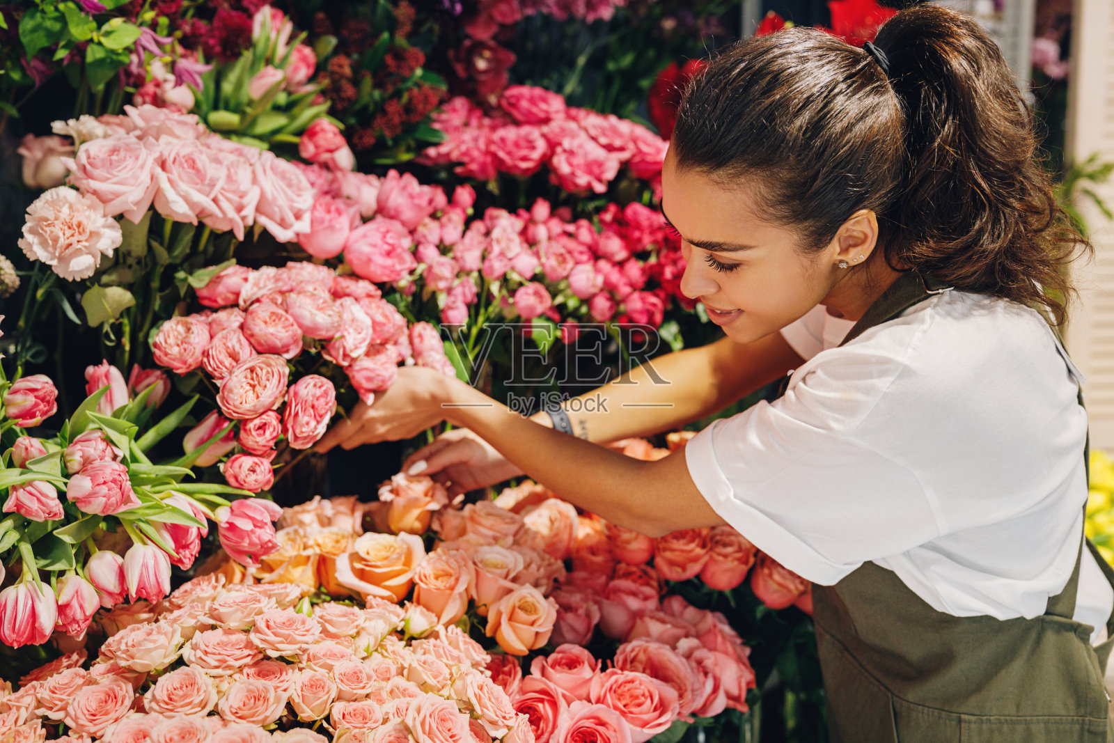 在花店工作的年轻女子。女性花商选择鲜花。照片摄影图片