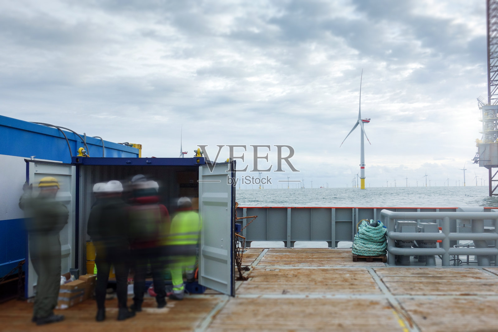 上午，技术人员站在中转船甲板上准备海上项目设备，海上风电场和海上平台在后面照片摄影图片
