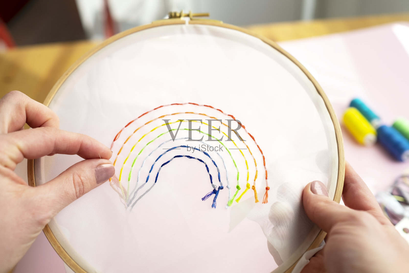 女用手缝制彩虹小绣图案在木框上，彩色的线在背景上照片摄影图片