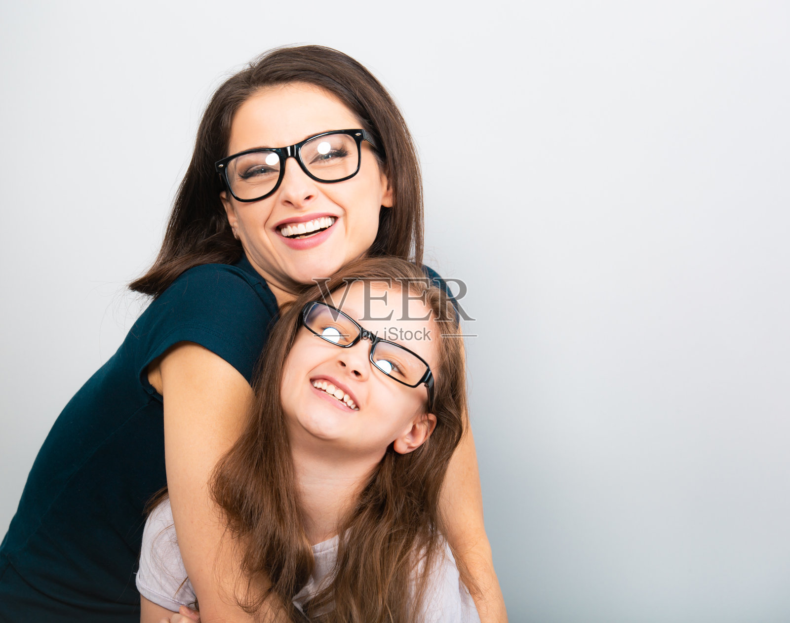年轻的露齿微笑的母亲和享受孩子的眼镜拥抱在浅蓝色的背景。特写镜头工作室肖像。教孩子呆在家里。在线教育照片摄影图片
