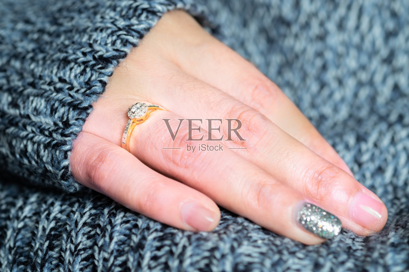 金色的结婚戒指或订婚戒指在女人的手指上的特写与深蓝的毛衣冬天的衣服背景。结婚或庆祝的礼物。柔软和选择性聚焦。爱和婚礼的概念。照片摄影图片