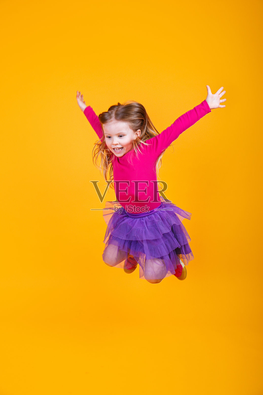 可爱的小女孩是跳跃和微笑在黄色的背景照片摄影图片