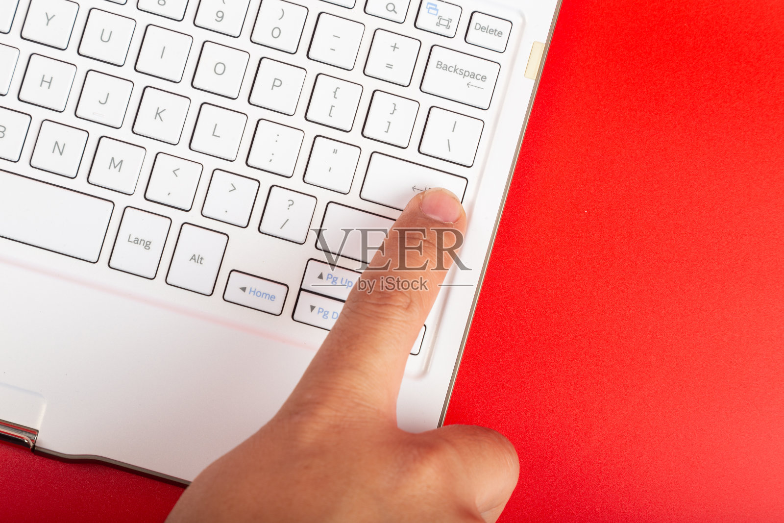 男人的手按ENTER键在白色键盘上孤立的红色背景。照片摄影图片