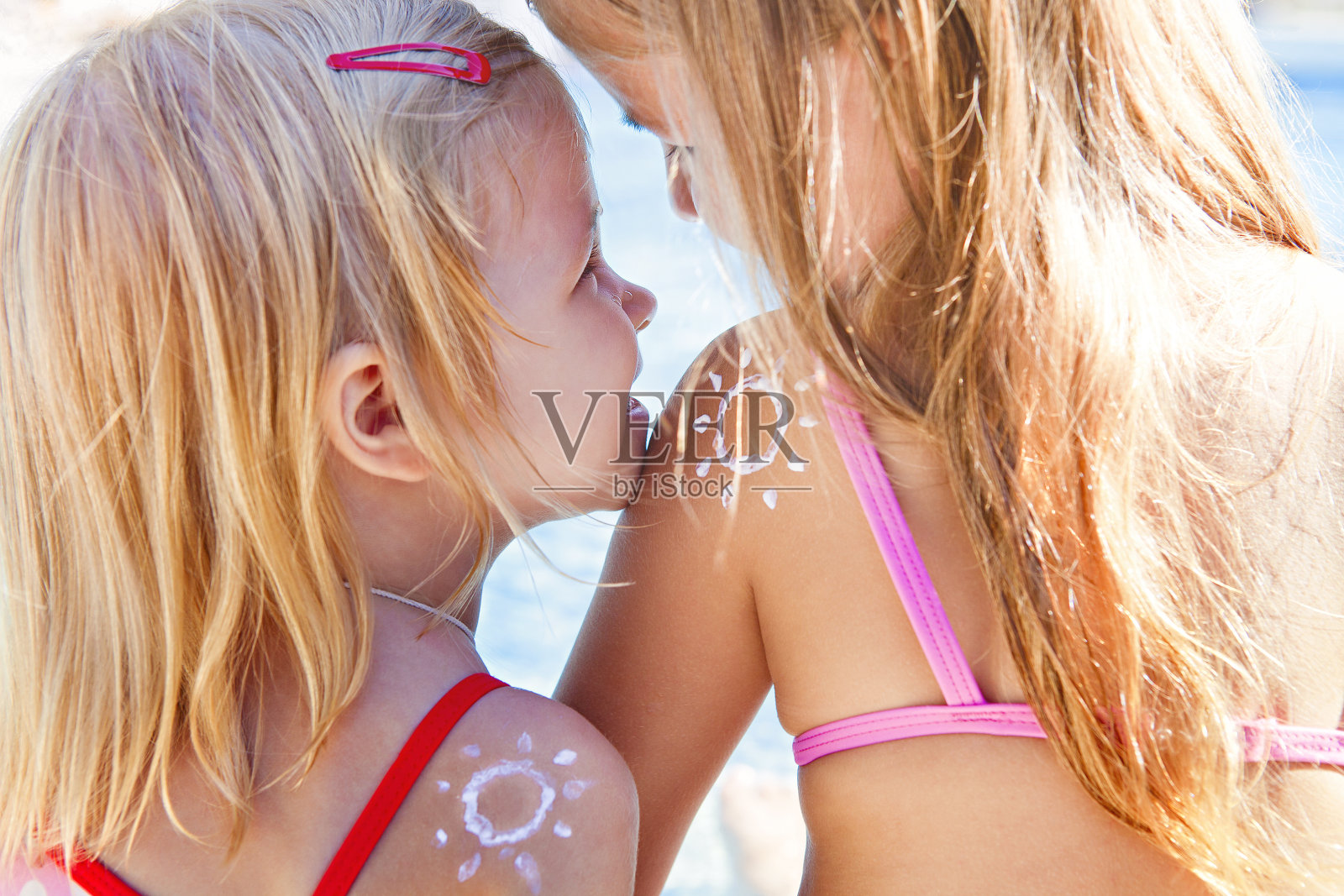 肖像快乐的金发女孩姐妹与奶油在肩膀的形状太阳笑和拥抱在日落照片摄影图片