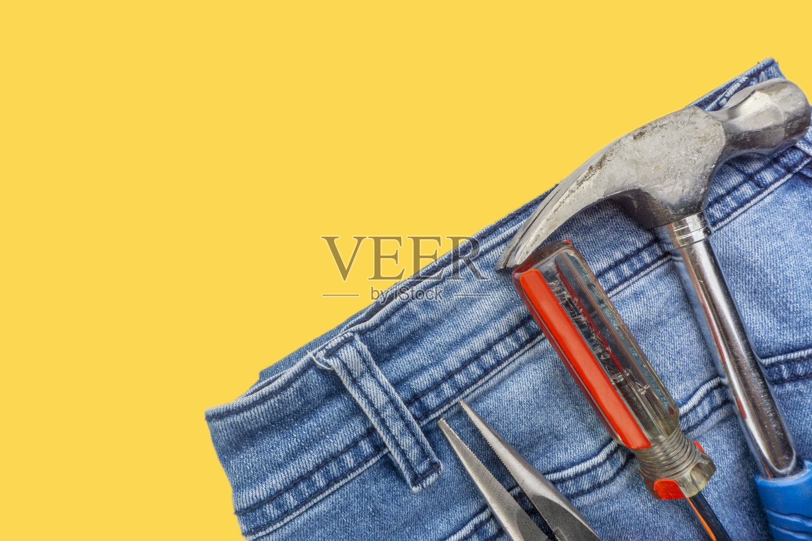 牛仔裤，螺丝刀，锤子和钳子在黄色的背景。照片摄影图片