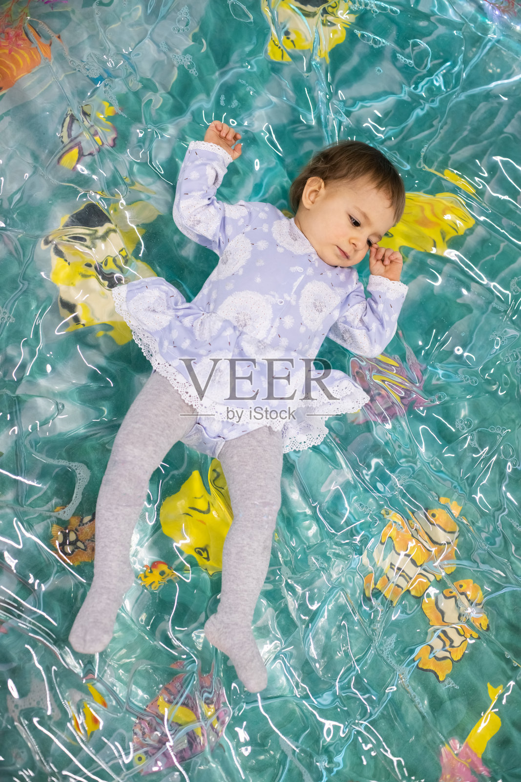在儿童游戏中心的儿童游乐场里，一个疲惫的小女孩穿着裙子躺在一个玩具塑料水池里。从上面的观点照片摄影图片