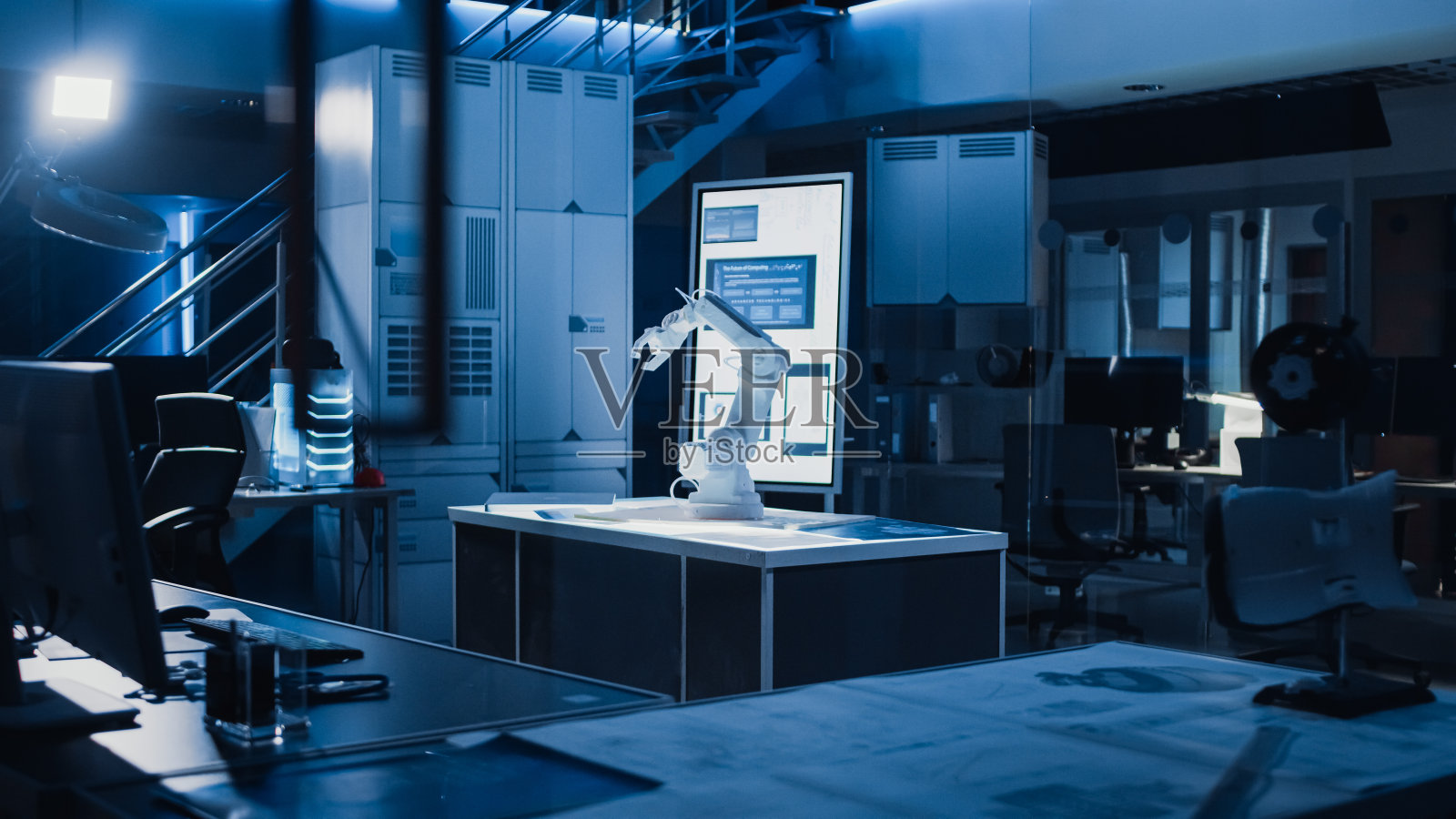 工业机器人设计研究实验室:机器人手臂原型站在桌面照明。在黑暗的背景中各种高科技设备，计算机，数字白板和蓝图照片摄影图片