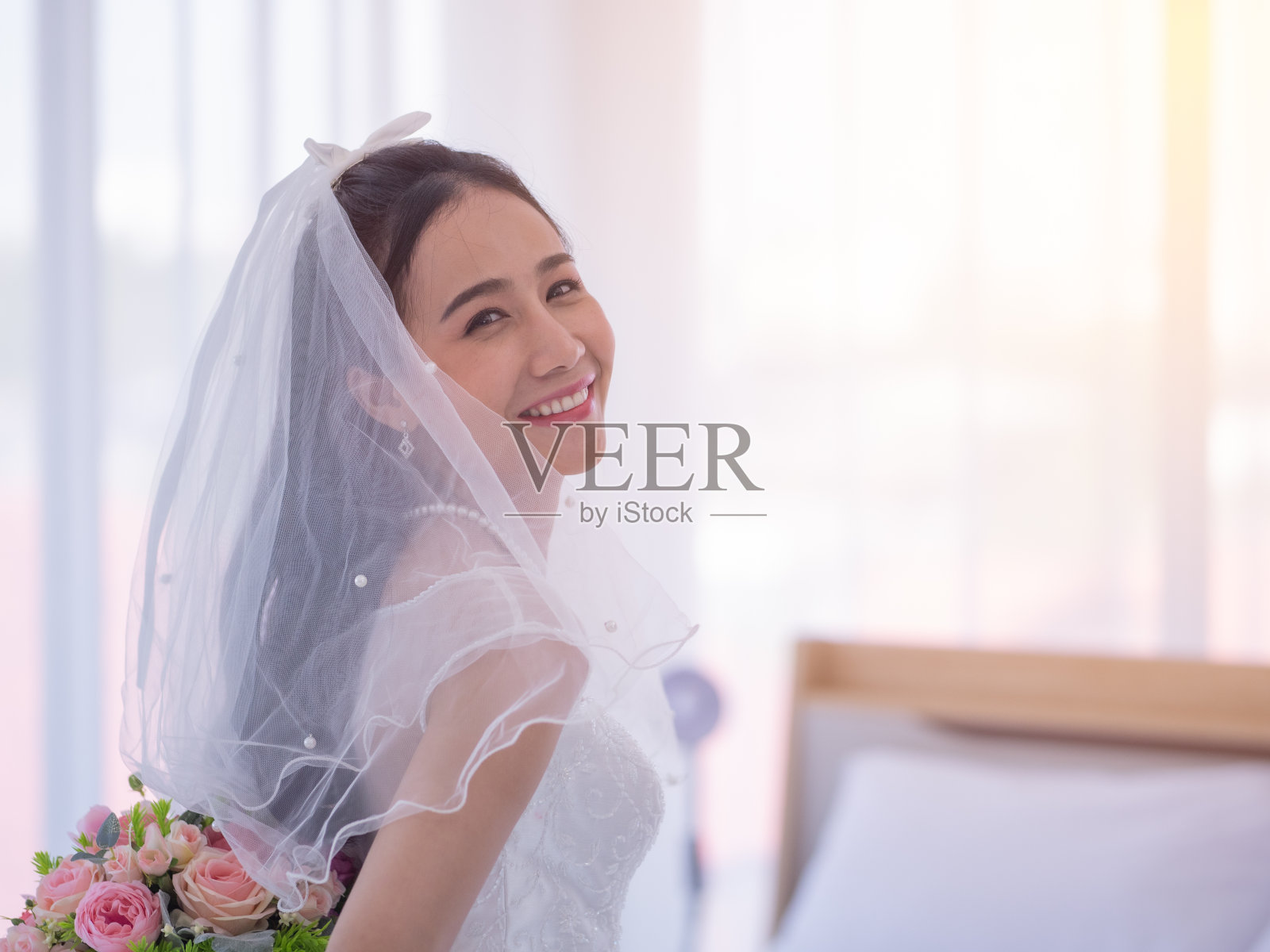 新娘手捧新娘花束站在后面，在化妆室里开心地笑着。为婚礼做准备。照片摄影图片
