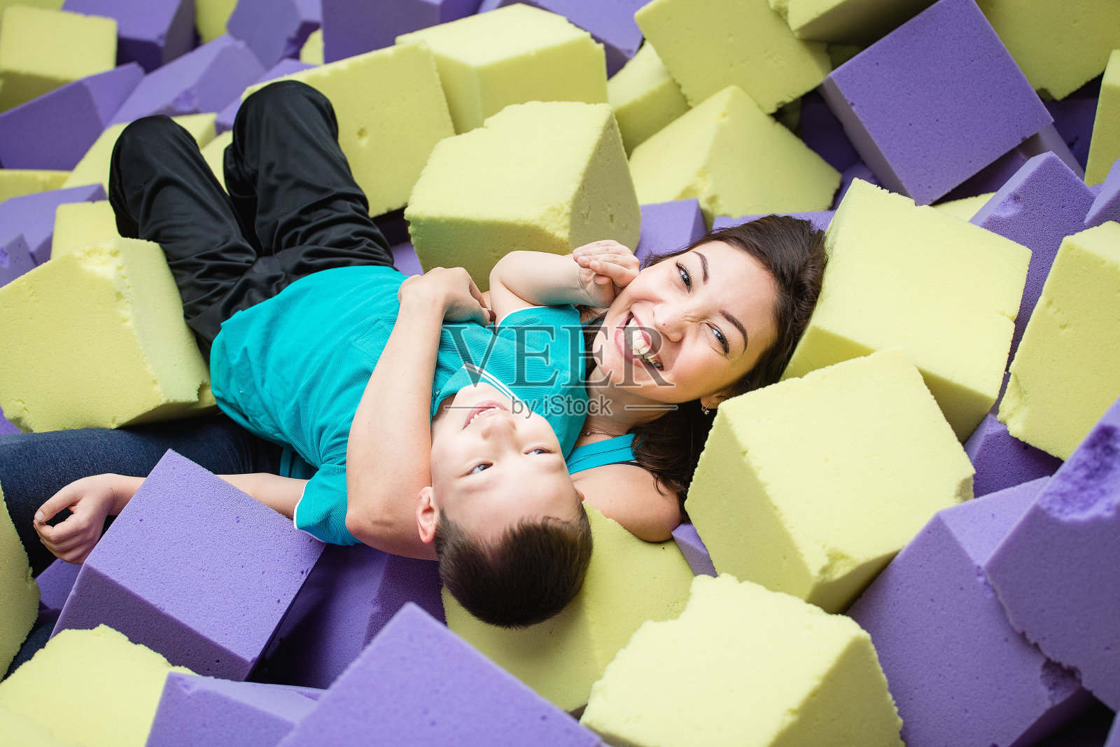亚洲母亲和她的儿子在室内游乐场玩积木。照片摄影图片