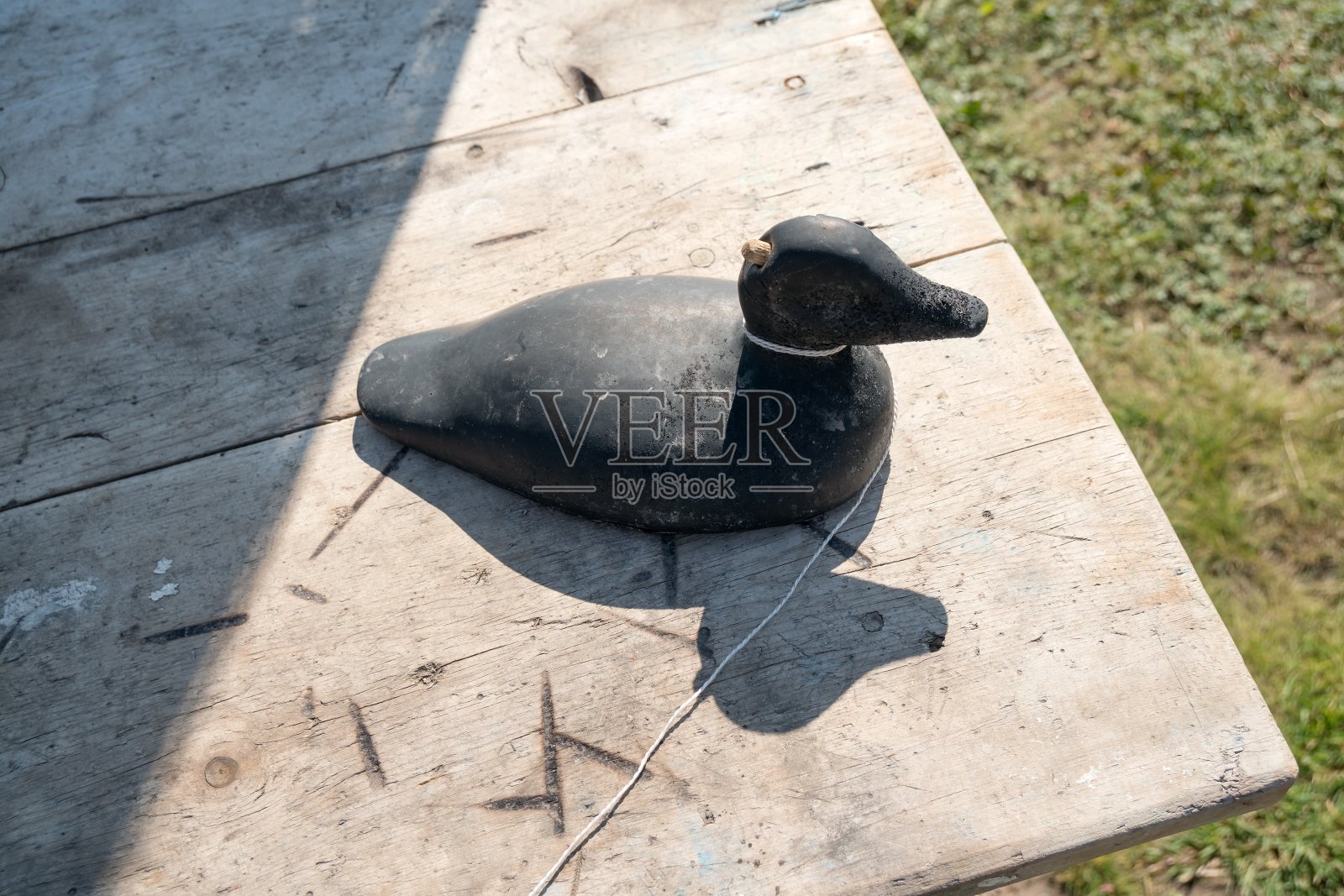 木制的鸭子诱饵站在一张桌子上，以草地为背景。照片摄影图片