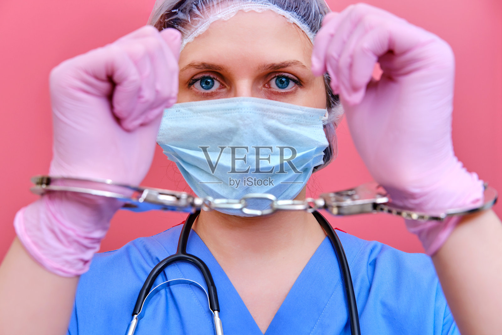 一个护士在一个粉红色的背景显示手戴手铐，特写。医生因贿赂病人被捕，概念照片摄影图片