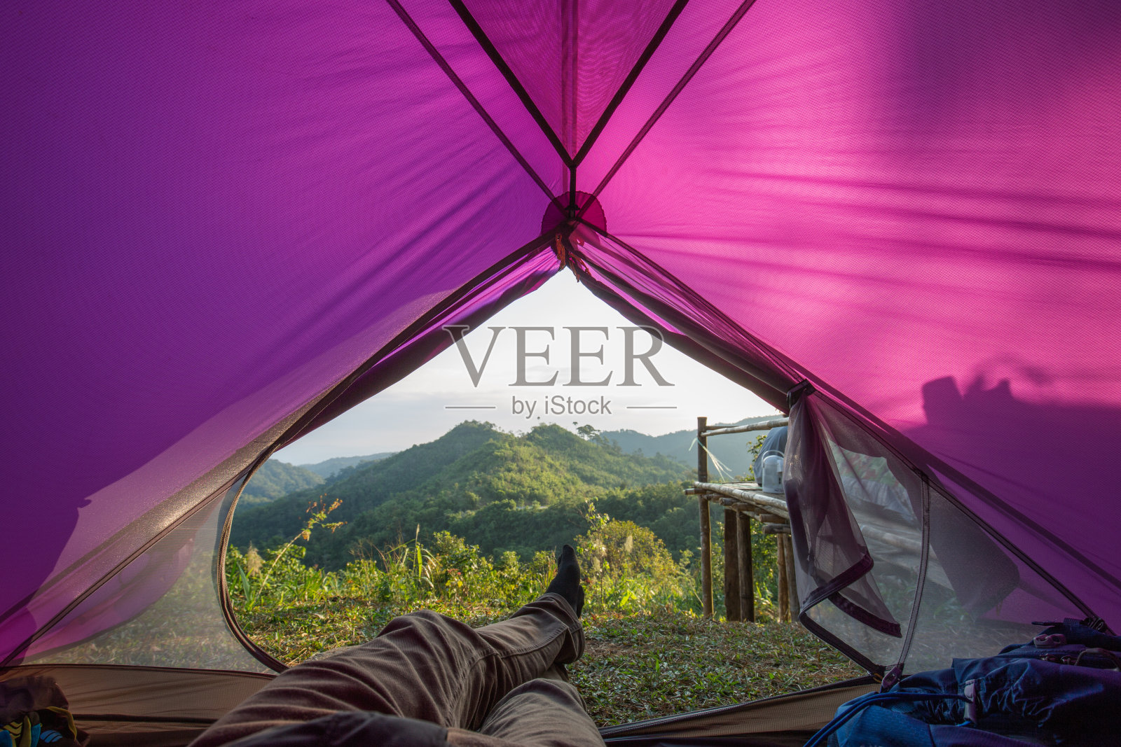男人穿着长裤躺在紫色的帐篷里看山景照片摄影图片