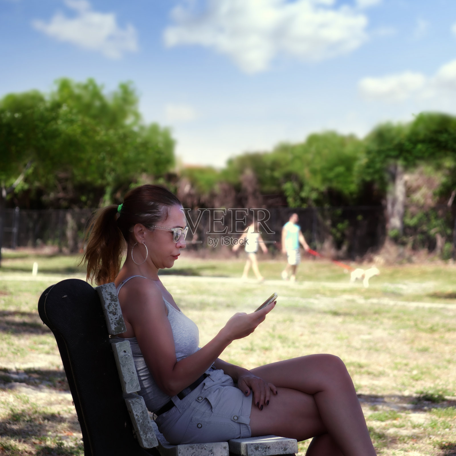 中年妇女坐在公园长凳上玩手机照片摄影图片