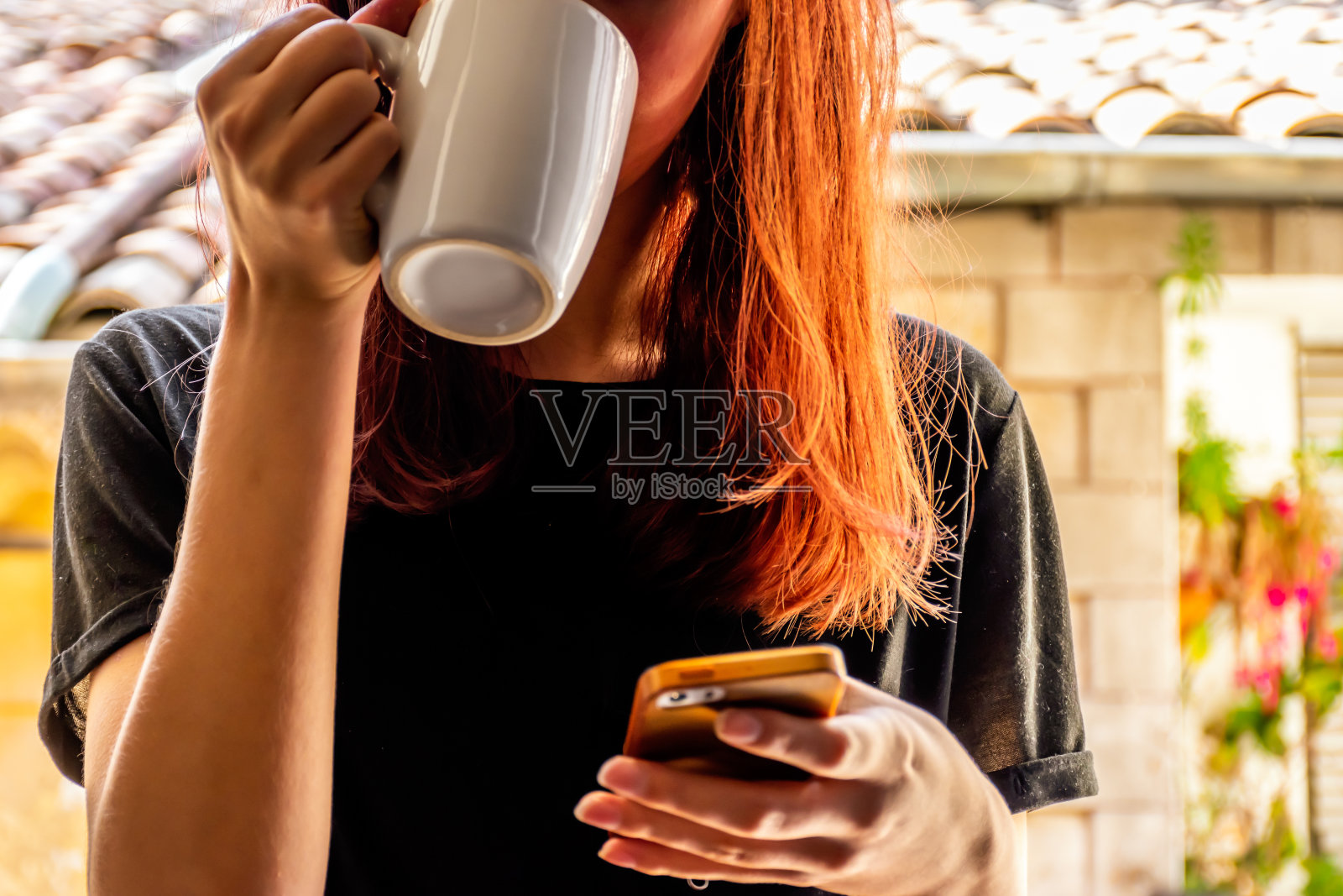 这是一个特写镜头，一个不认识的年轻白种人红发女人喝着一杯热饮，低头看着她的智能手机，背景是一座古老的法国建筑照片摄影图片