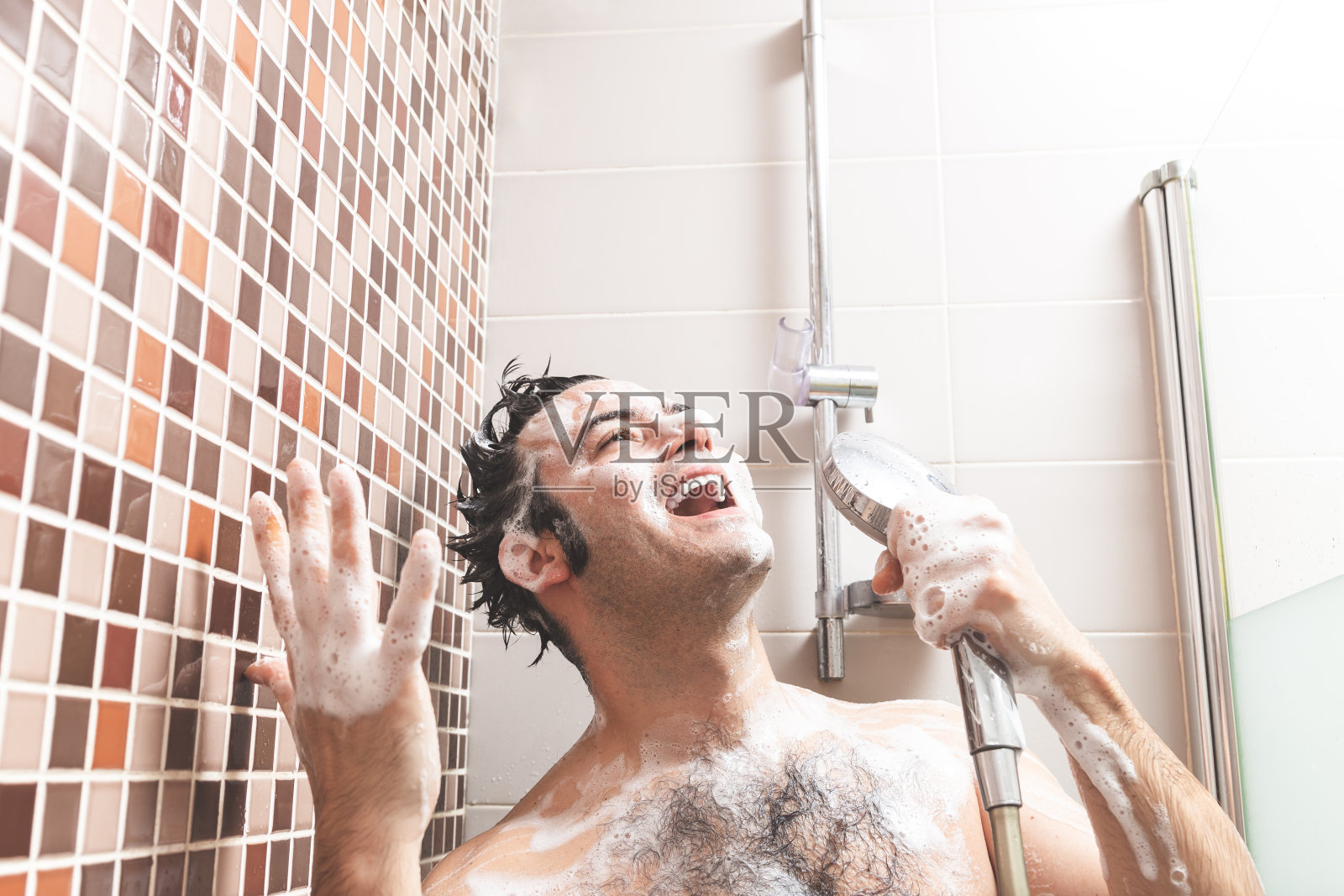 年轻的白人男子，唱歌和手势愉快充满香皂在浴室淋浴。照片摄影图片