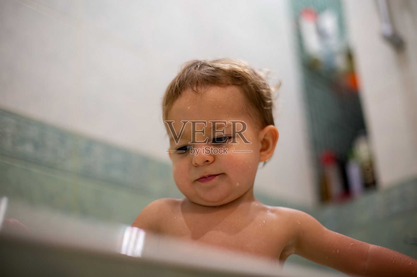 可爱的小婴儿在浴缸里洗澡。以一个模糊的特写，软焦点，底部视图的绿色浴室为背景照片摄影图片