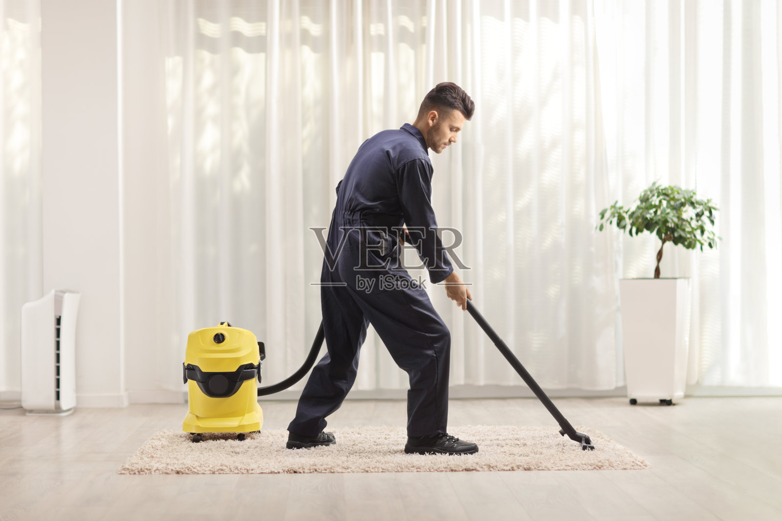 一个穿制服的男人在屋里用吸尘器吸地毯照片摄影图片