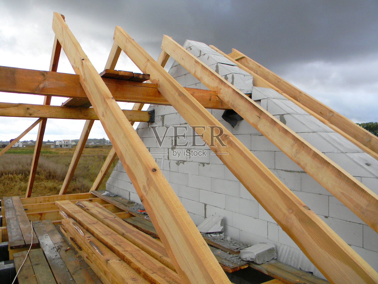 未完成的房屋框架屋顶施工与雨云在天空。湿屋顶横梁。照片摄影图片