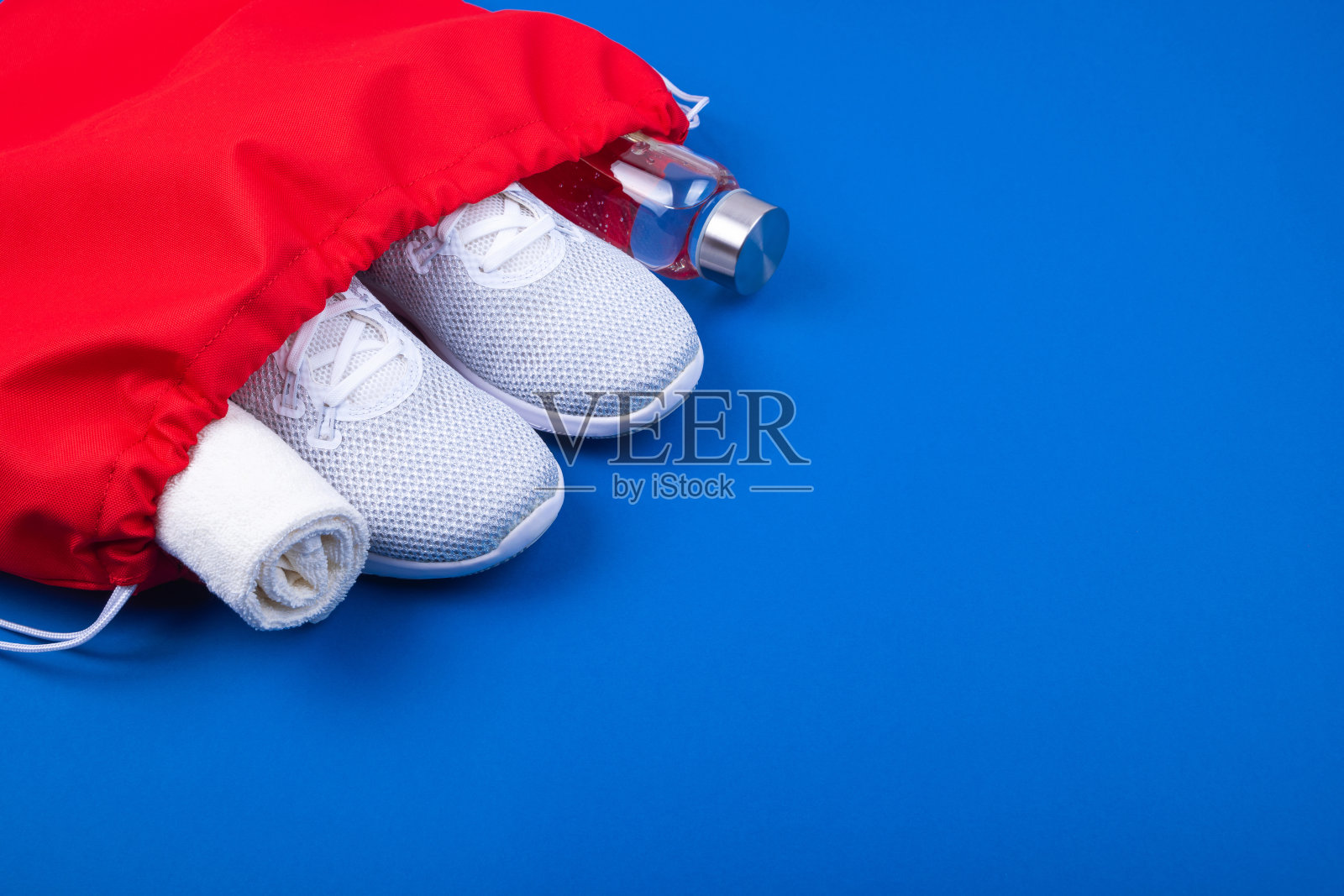 白色运动鞋，玻璃水瓶和毛巾在红色的运动包在青蓝的背景。照片摄影图片