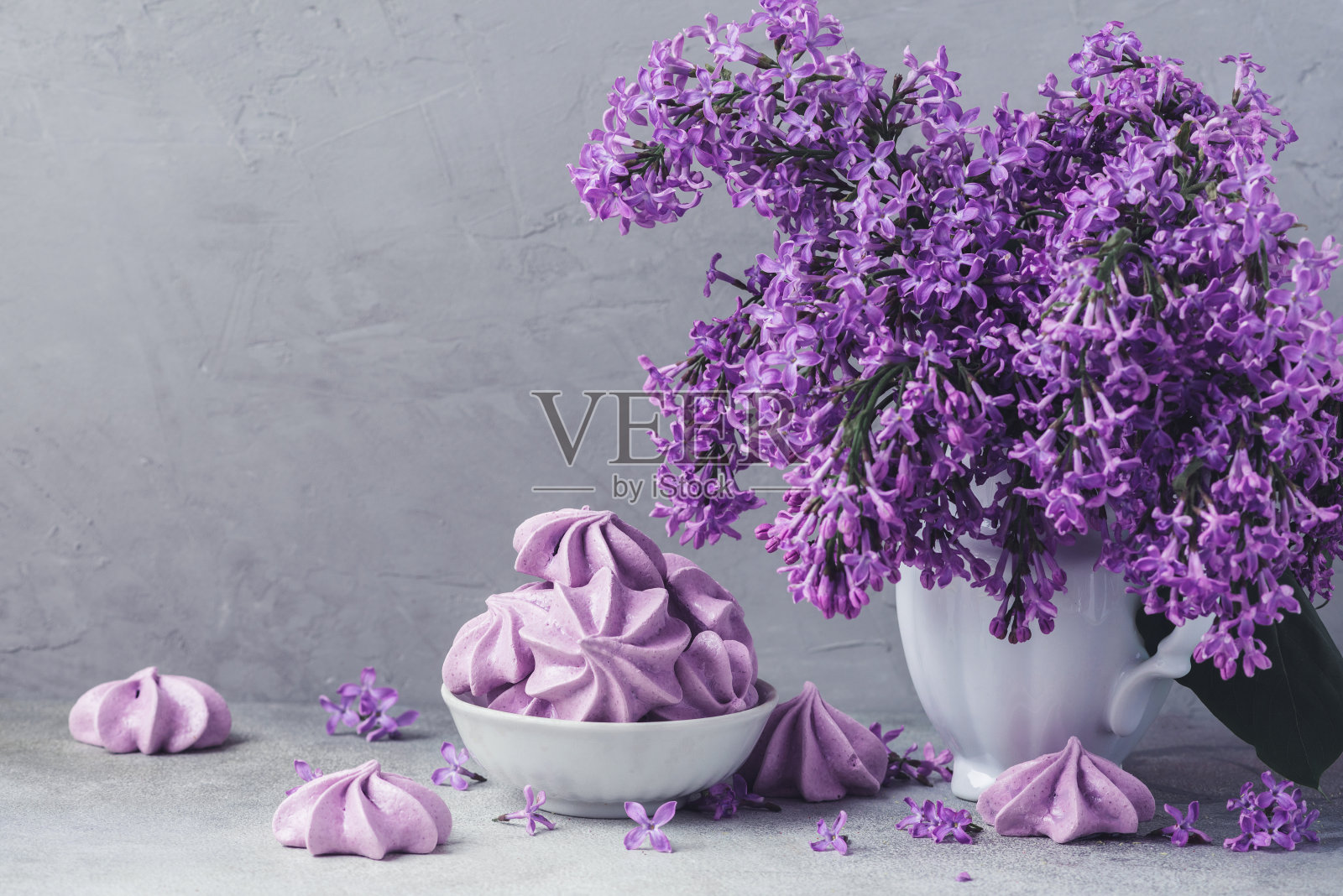 花瓶里的丁香花和混凝土背景上的紫色蛋白饼干的静物画。复古或instagram色调照片摄影图片