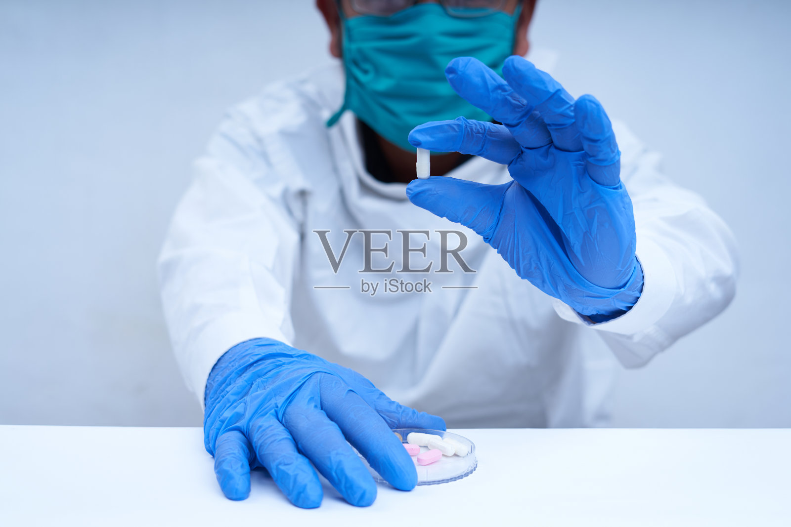 在药物研究实验室里，戴着防护面具，手指戴着手套拿着药丸的男科学家照片摄影图片