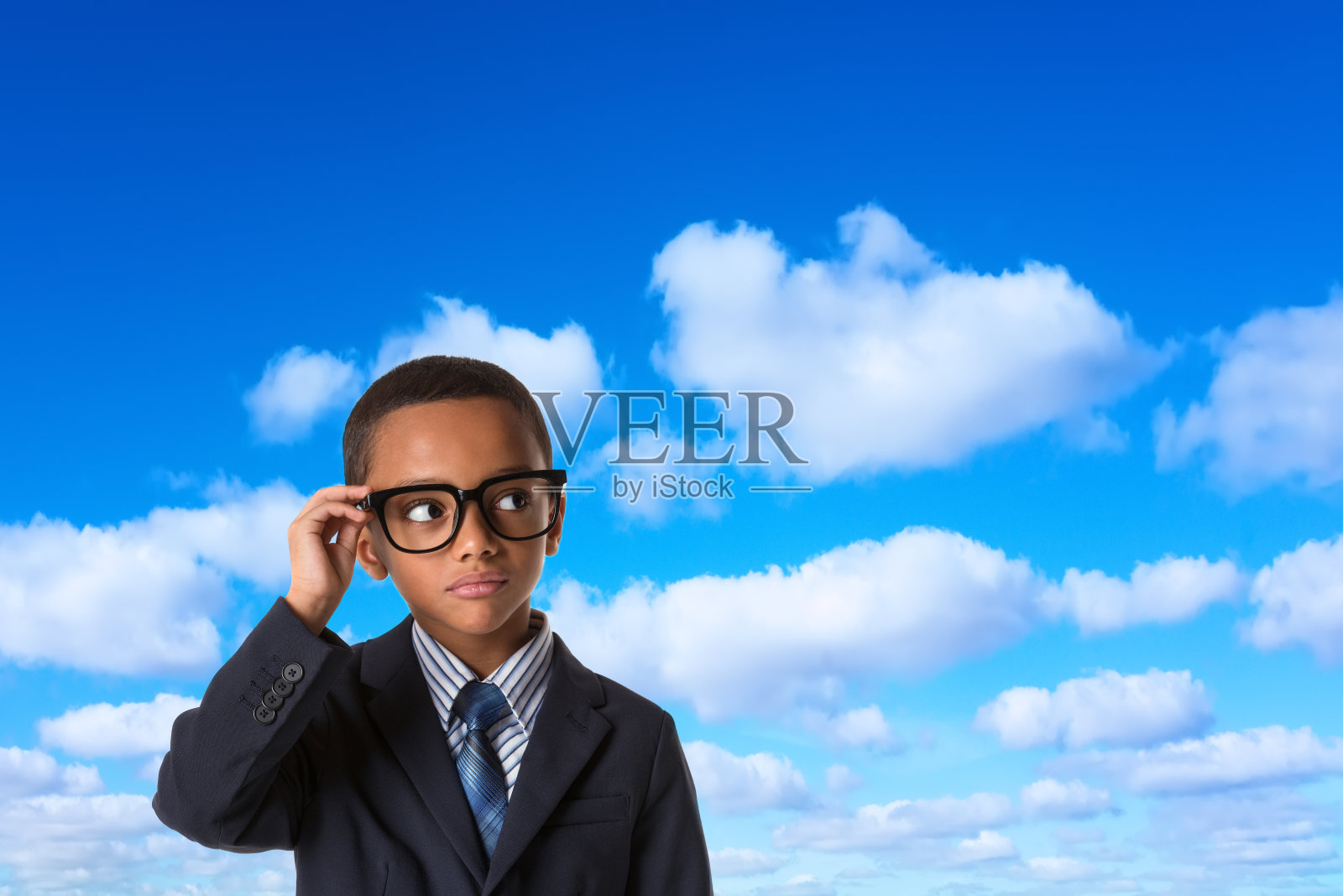 领导和成功的概念-深思熟虑的非洲裔美国男孩穿着西装，戴着眼镜在蓝天的背景。照片摄影图片