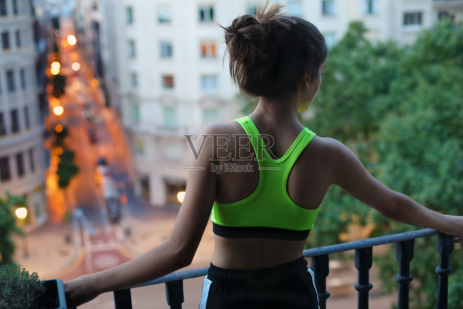 小女孩穿着运动服，倚在阳台上，望着大街，在隔离区里照片摄影图片