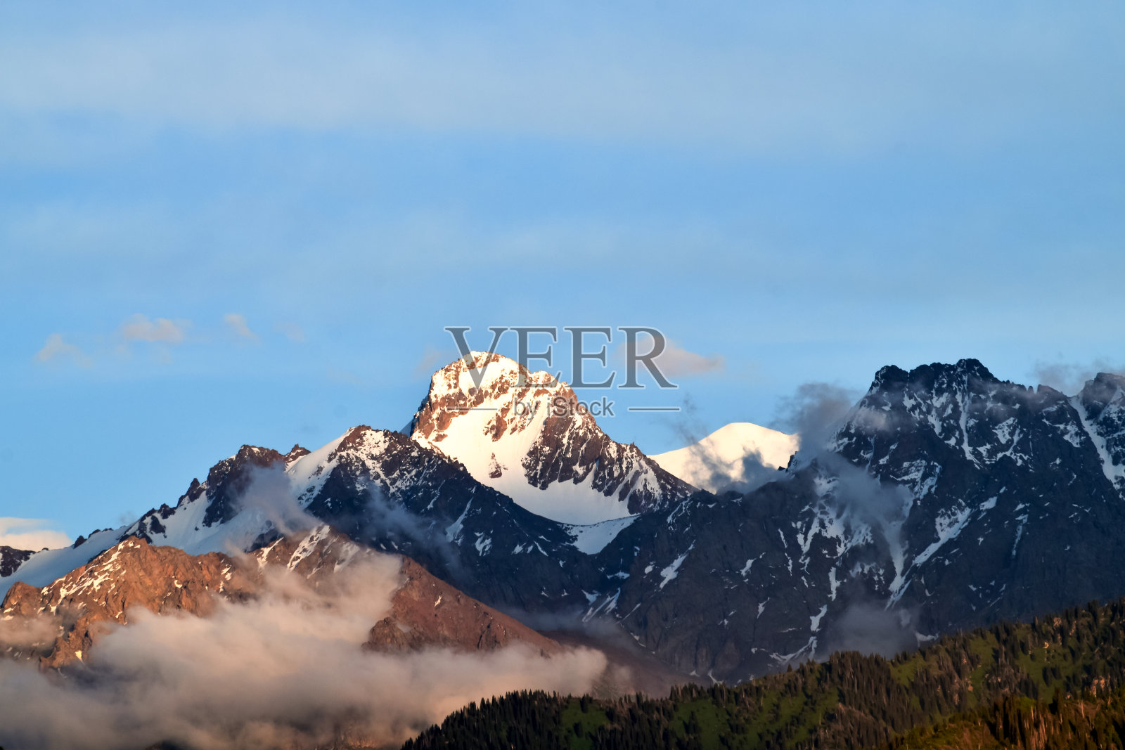 山峰在旭日的余晖中达到顶峰。云中有雪的山。照片摄影图片