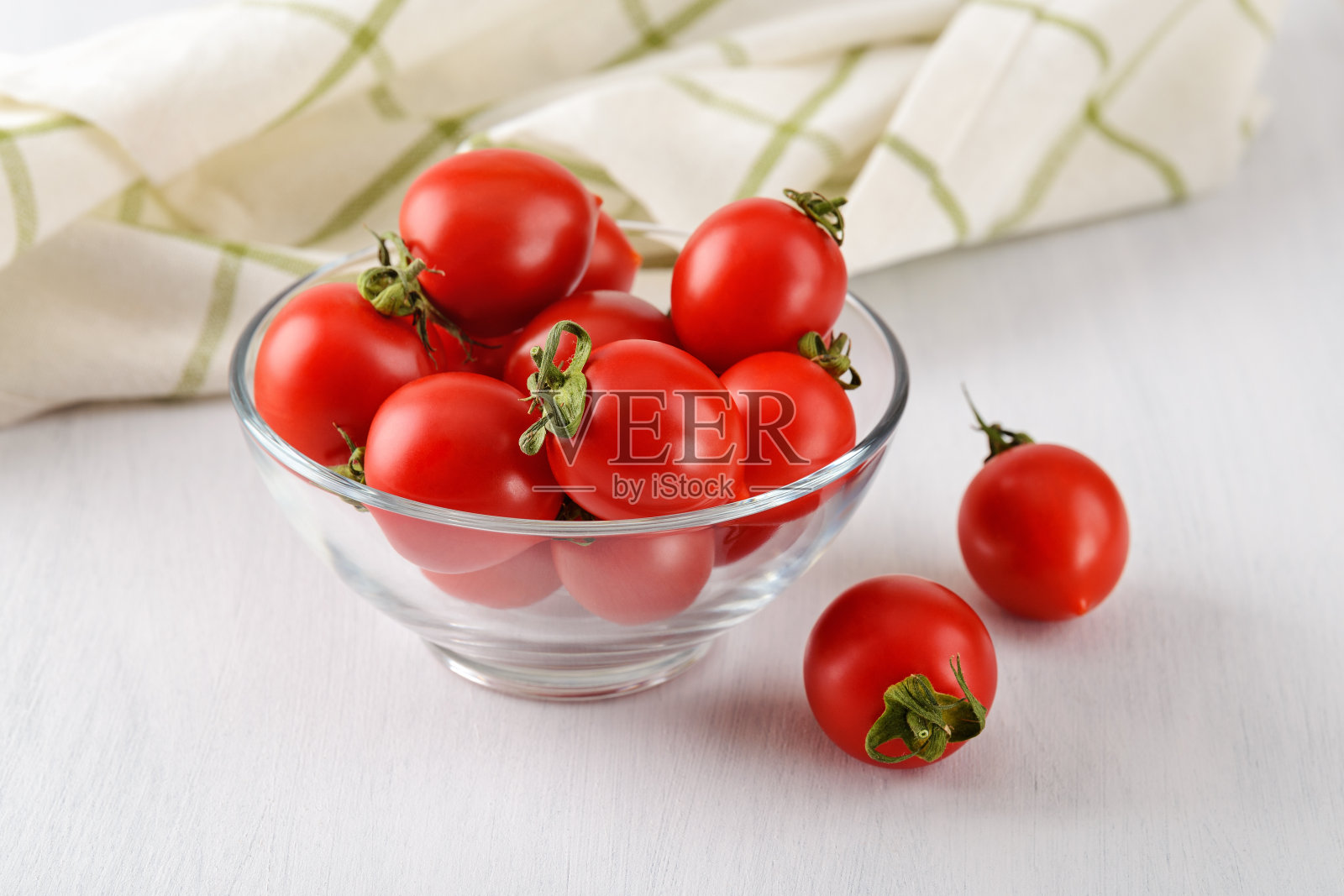 整个成熟的红色樱桃番茄放在一个玻璃碗里，放在质朴的白色餐桌上。蔬菜，素食和健康饮食。生食饮食。照片摄影图片