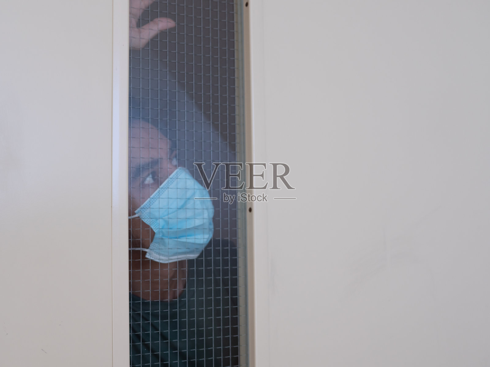 一个戴医用面具的孤独男人透过窗户看照片摄影图片