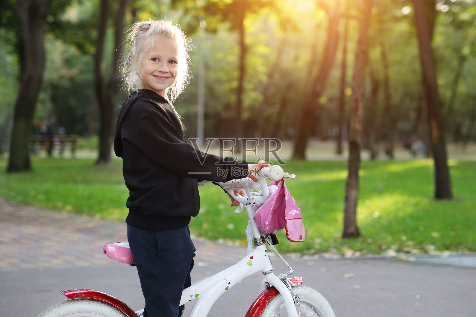 可爱可爱美丽的白人小女孩喜欢骑白色的小自行车在绿色的夏天城市公园森林或花园在明亮的阳光灿烂的一天户外。儿童健康生活方式概念照片摄影图片