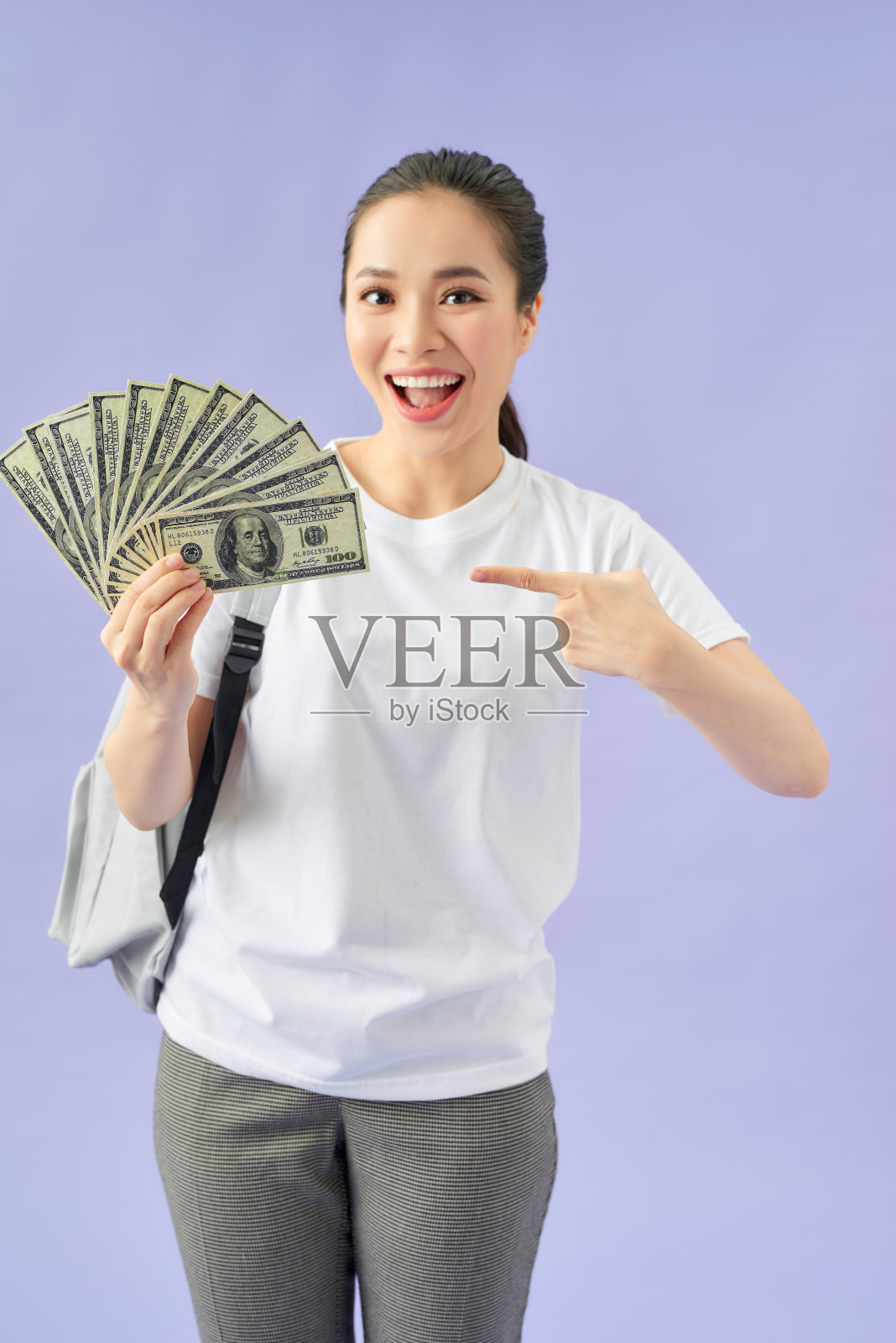 惊奇的女学生拿着扇子里的现金在美元钞票做胜利者的手势照片摄影图片