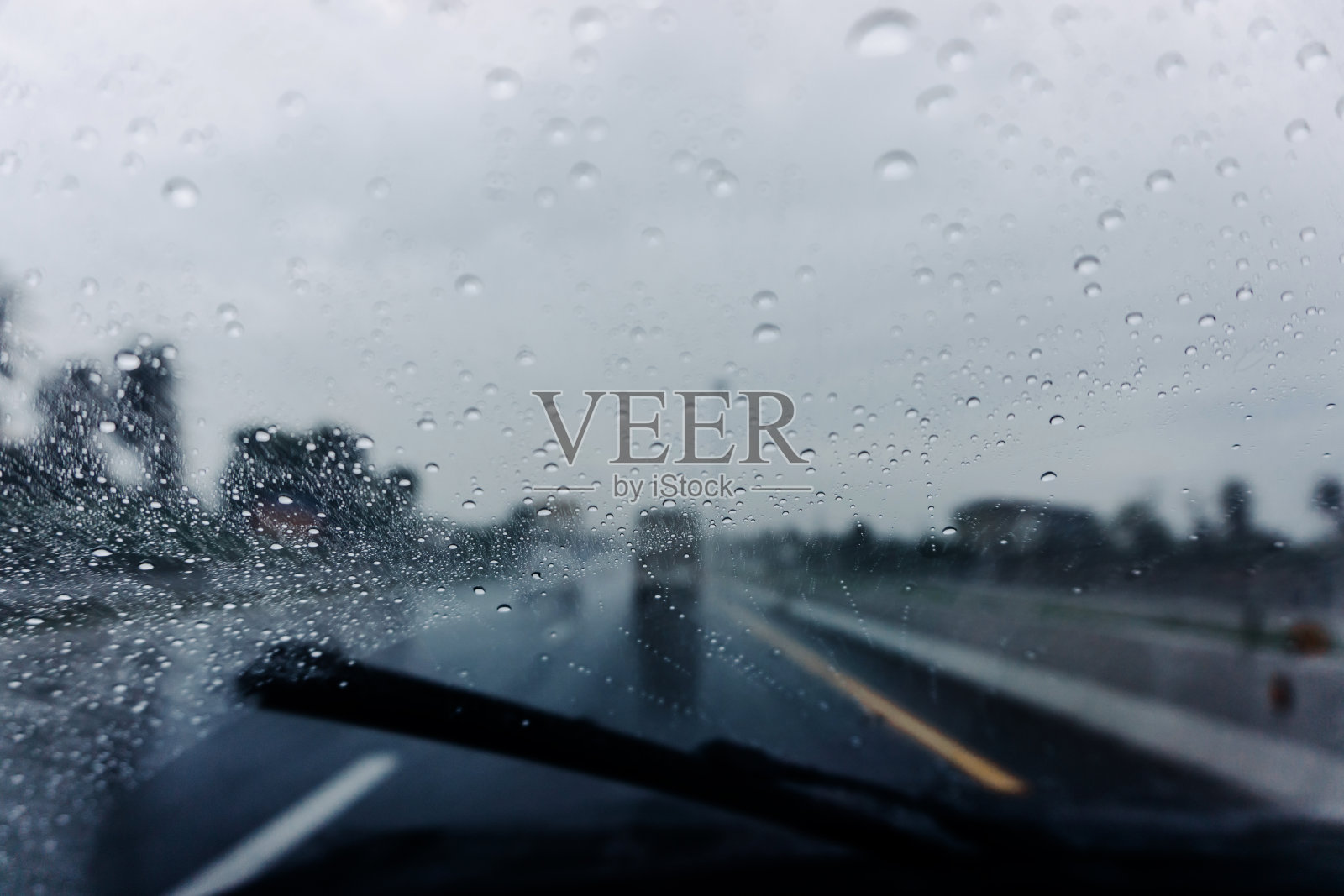 雨滴落在汽车玻璃上。汽车在下雨时在潮湿的道路上行驶。照片摄影图片