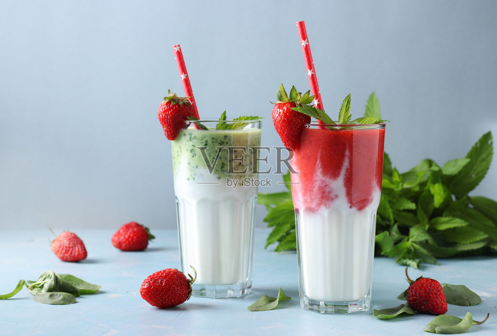 两个健康的排毒奶昔与新鲜的草莓，菠菜，薄荷和酸奶在浅蓝色的背景与新鲜的成分，饮食和减肥控制概念，特写照片摄影图片