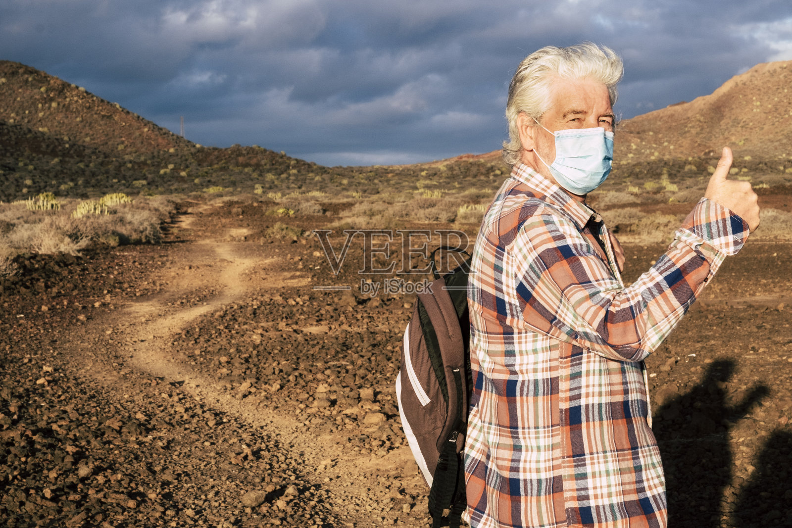 后视图:一位老人走在台阶上，享受自然，因冠状病毒封锁后首次离家。干旱的景观和地平线上的山脉。照片摄影图片