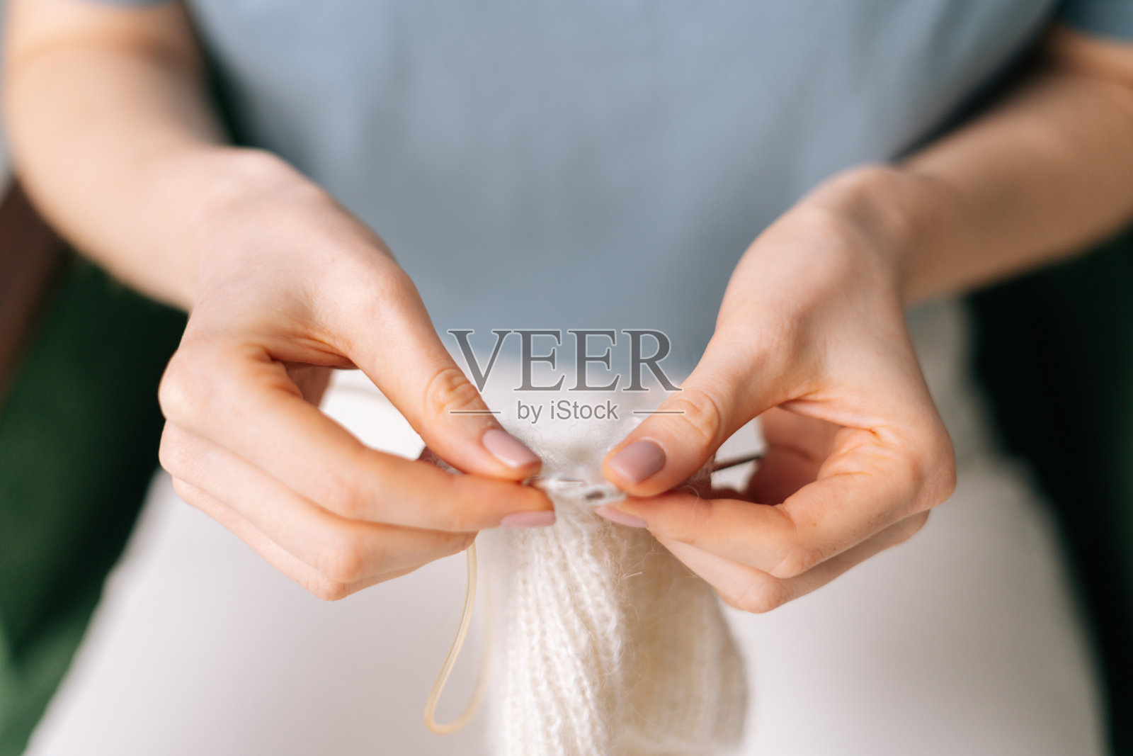 近的手，不可辨认的妇女编织手工衣服辐条使用白色羊毛。照片摄影图片