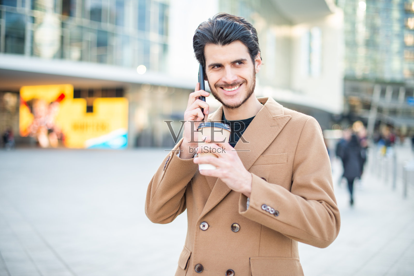 一个男人一边打电话一边拿着一杯咖啡走在城市里照片摄影图片
