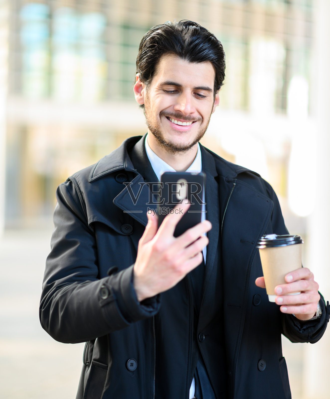 英俊优雅的穿着男子使用他的智能手机，拿着一杯咖啡照片摄影图片