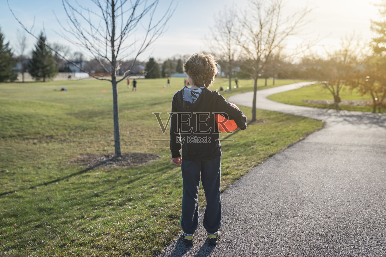 一个在公园里抱着一个亮橙色足球的孩子的后视图照片摄影图片