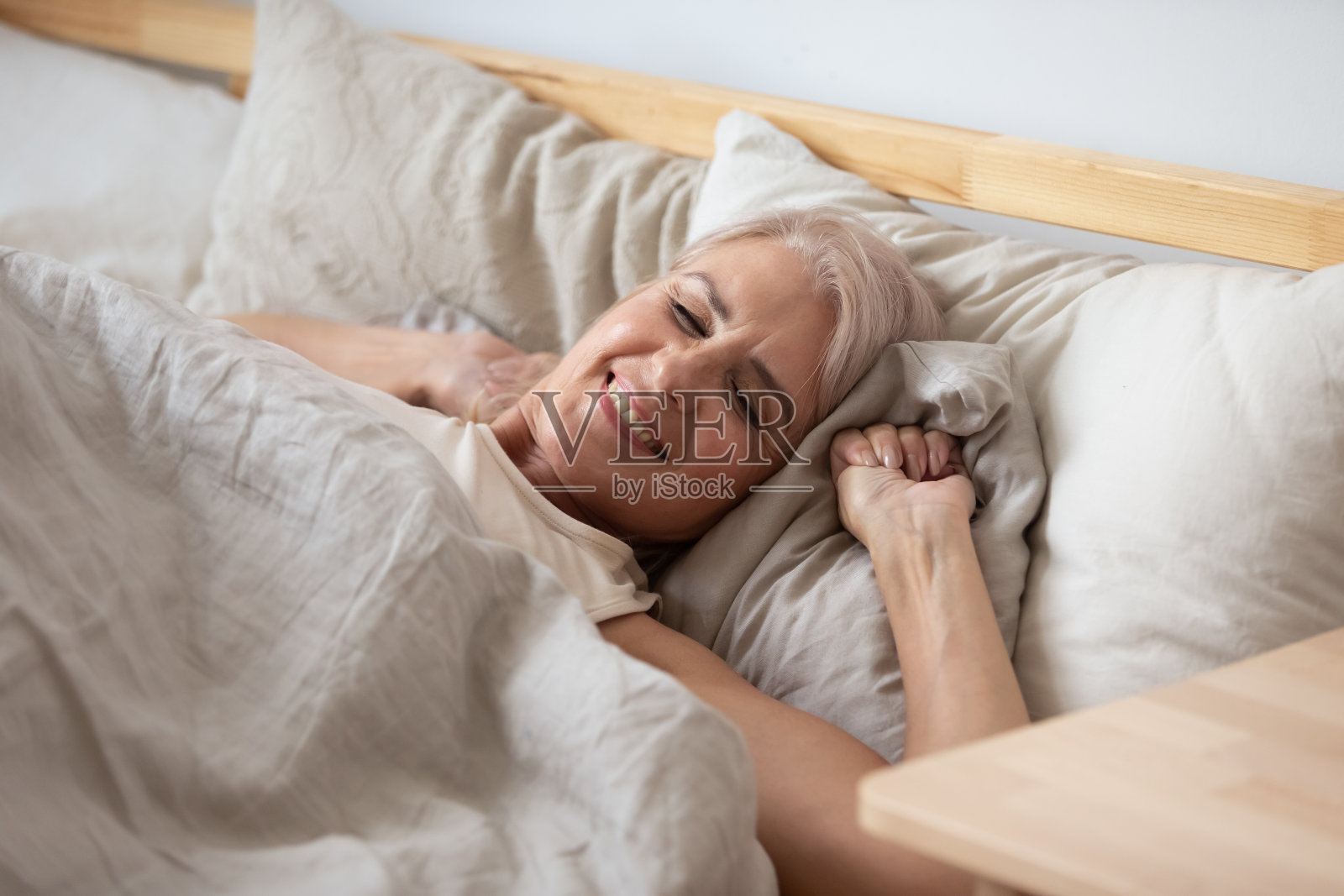 微笑的中年退休妇女在舒适的床上醒来。照片摄影图片