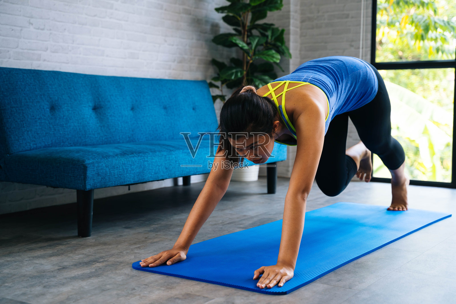 强壮的健身女孩在运动服装做平板支撑锻炼。亚洲妇女在家训练在她的客厅舒适的沙发家庭内部设置。照片摄影图片