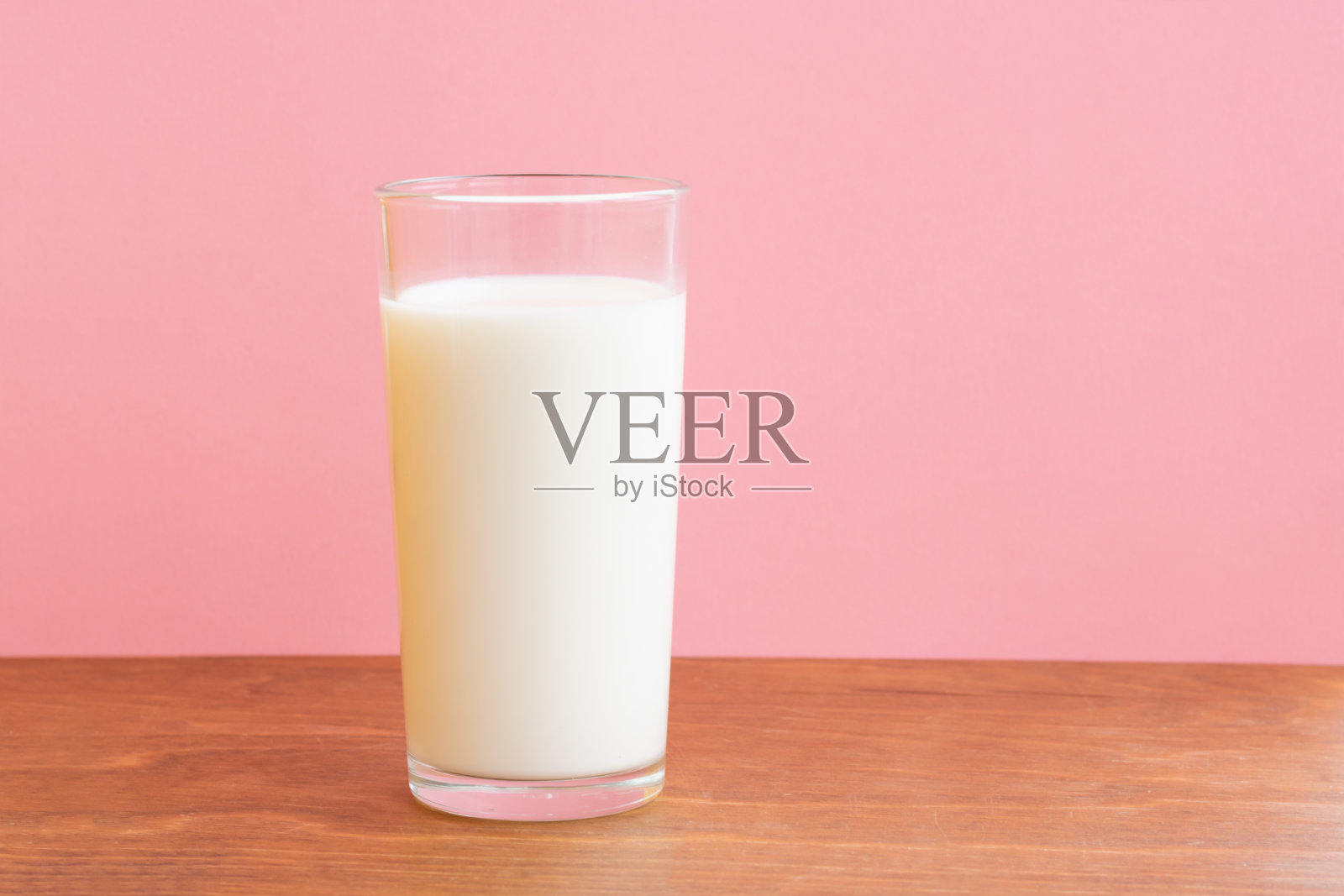 粉红背景的木桌上放着一杯鲜奶。单一对象照片摄影图片