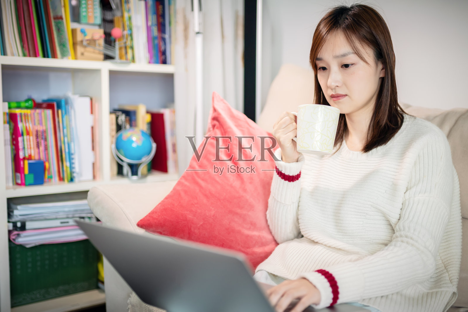 年轻女子坐在沙发上用笔记本电脑喝着咖啡照片摄影图片