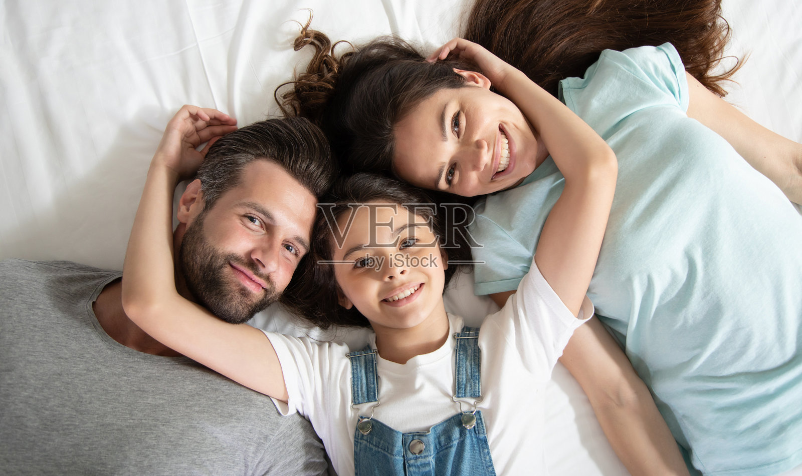 俯视图的照片，一个美丽的幸福的家庭躺在床上，有乐趣，而他们看着相机照片摄影图片