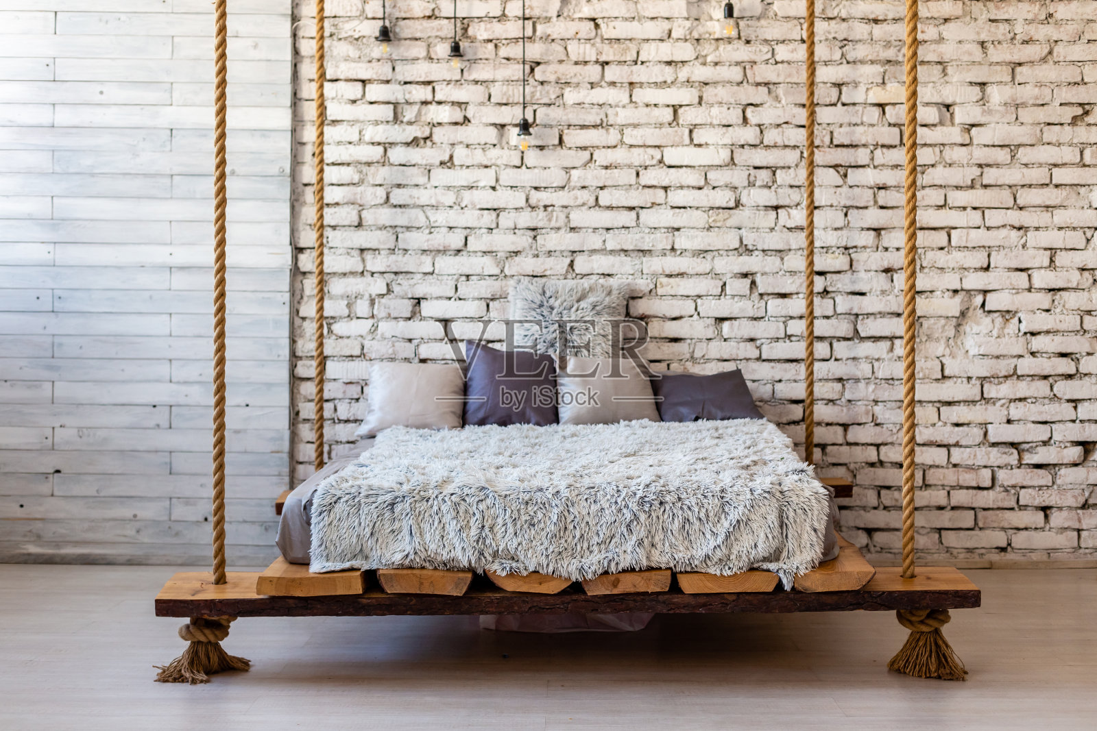有枕头的木床和毛皮毯子挂在绳子上的阁楼内部时尚的现代卧室。粗糙的斯堪的纳维亚豪华家具风格。照片摄影图片