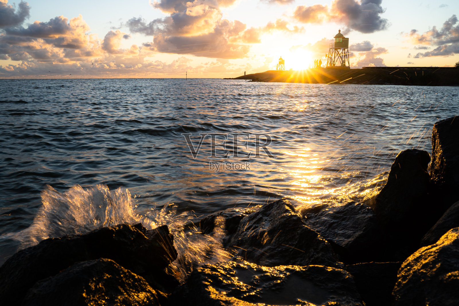 海岸上溅起水花，背景是灯光和壮观的日落照片摄影图片