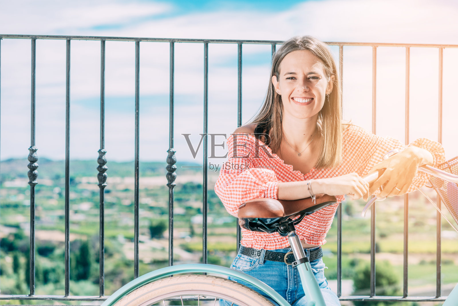 年轻微笑的女子骑着自行车，坐在美丽的风景的背景照片摄影图片