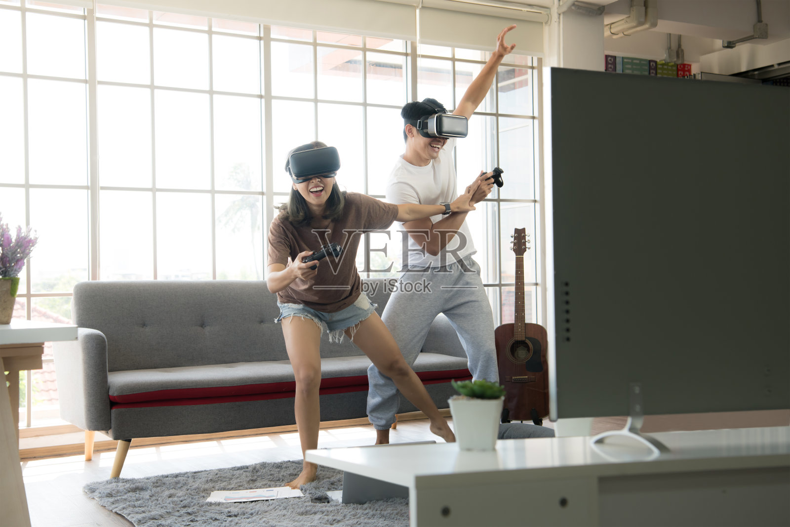年轻快乐的亚洲夫妇戴着虚拟现实眼镜在他们的公寓里玩电子游戏照片摄影图片