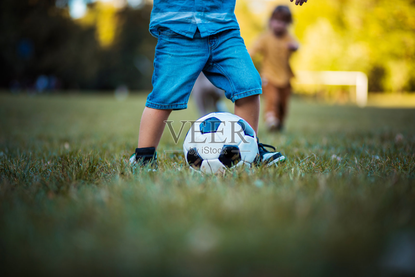 小男孩的腿在草地上踢足球。照片摄影图片