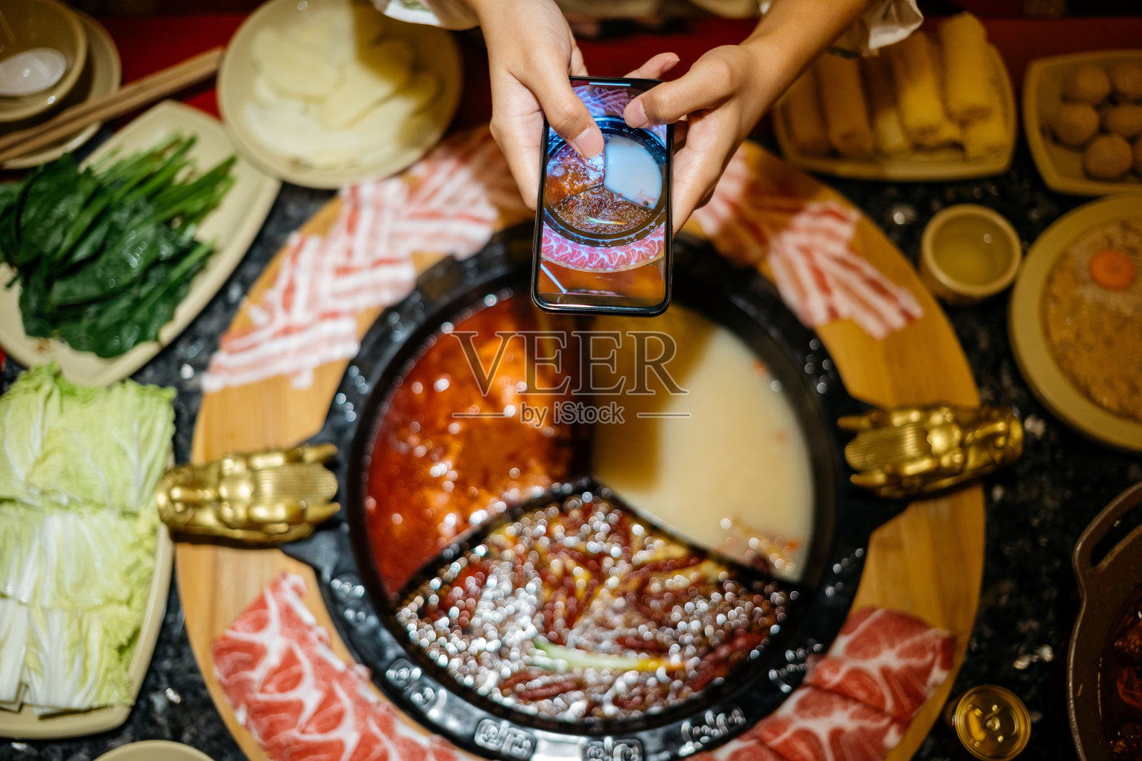 一名亚洲中国女性正在用智能手机拍摄她的火锅晚餐照片摄影图片